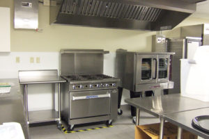 The updated kitchen for Rockdale Temple. A six-burner, stainless steel stove is center, and to the right is a holding cabinet. Lots of stainless steel counters can be seen.