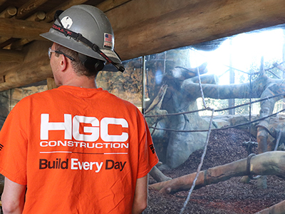 A construction worker stands in front of a large glass wall reveals a habitat for gorillas.
