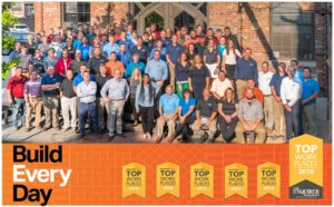 More than fifty HGC employees, diverse range of age, gender, and race, standing outside and smiling, with a banner displaying history of Top Workplace awards, including Top Workplace 2018