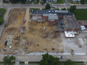 An aerial view of Amity Elementary from the back of the building. The East wing of the building has been demolished, and a variety of construction vehicles are at work smoothing the ground where the wing used to be. The West wing has an addition being added on, of which the first floor seems to be nearing completion.