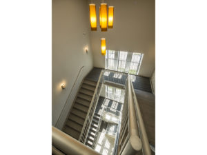Looking down on large stairwell. Modern accent light fixture adds a splash of warm color to the otherwise cool and gray space. Windows let in lots of natural light.